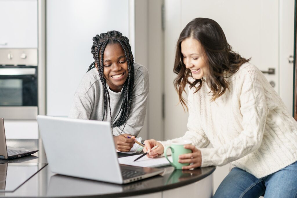 Two college girls studying together at home with laptops while drinking coffee